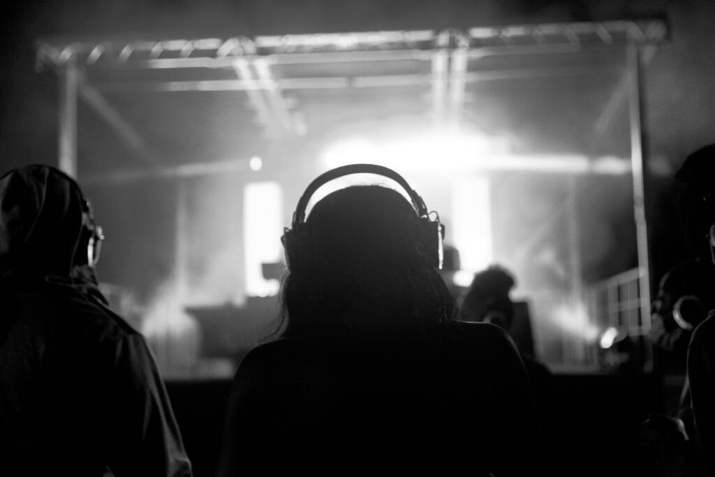 Backlit photo of a student participating in the Headphone Disco at George Mason University. The backlit student, who is entirely in shadow, is wearing a set of headphones. The light behind the student is a bright, neon blue and is coming from a DJ-stage set up for the disco.
